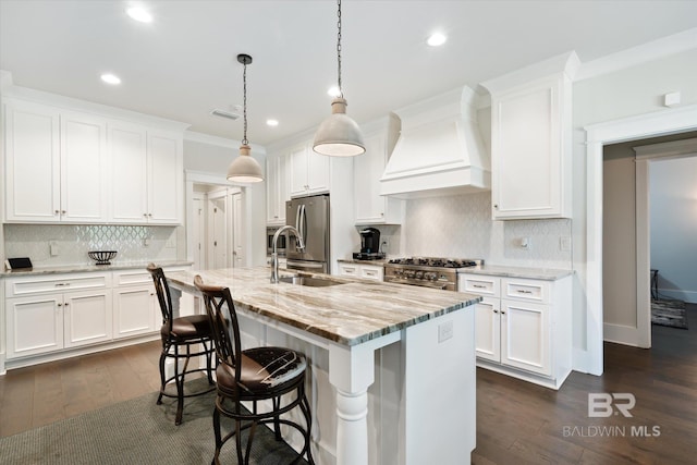 kitchen featuring a center island with sink, custom exhaust hood, white cabinetry, and decorative light fixtures