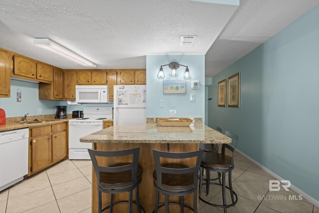 kitchen featuring light stone counters, a textured ceiling, white appliances, light tile patterned floors, and a breakfast bar area