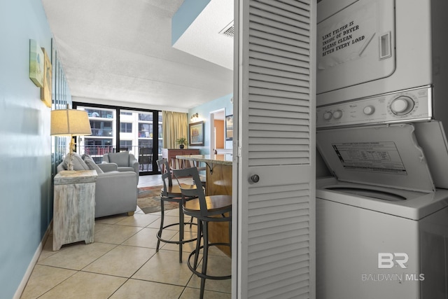 clothes washing area featuring light tile patterned floors, a textured ceiling, and stacked washer / dryer