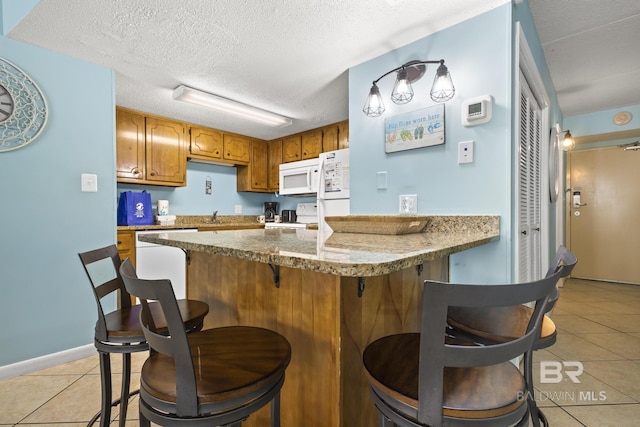 kitchen with stone counters, light tile patterned floors, white appliances, and a textured ceiling