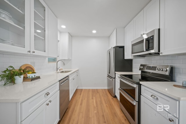 kitchen with backsplash, light wood-style flooring, appliances with stainless steel finishes, white cabinets, and a sink