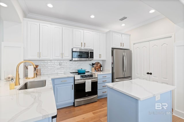 kitchen featuring appliances with stainless steel finishes, white cabinets, light hardwood / wood-style flooring, light stone counters, and sink