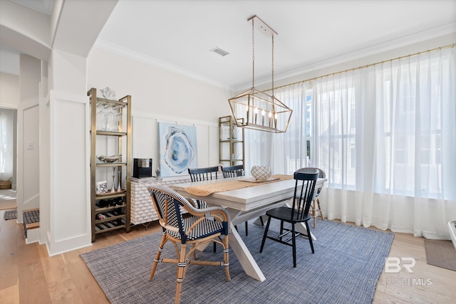 dining space featuring crown molding, light wood-type flooring, and an inviting chandelier