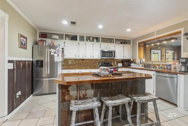 kitchen with a kitchen bar, appliances with stainless steel finishes, a textured ceiling, white cabinets, and a center island