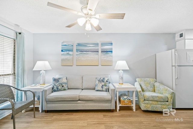 living room featuring ceiling fan, a textured ceiling, and light hardwood / wood-style floors