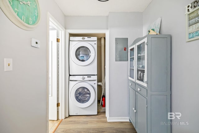 laundry area with electric panel, stacked washer and dryer, and light hardwood / wood-style flooring