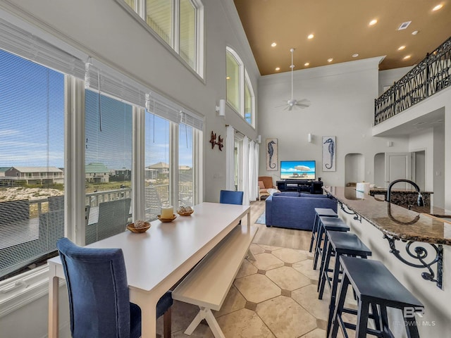 dining area featuring a towering ceiling, light hardwood / wood-style flooring, sink, and ceiling fan