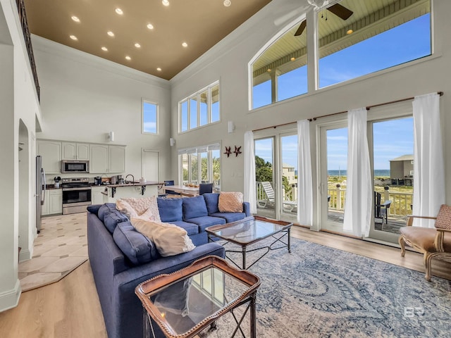 living room with ceiling fan, light hardwood / wood-style floors, and a towering ceiling