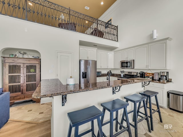 kitchen featuring white cabinetry, stainless steel appliances, a towering ceiling, and a breakfast bar area