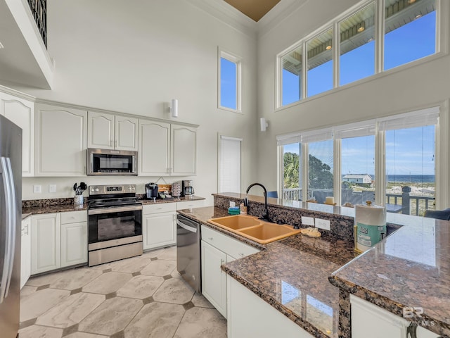 kitchen featuring a high ceiling, sink, dark stone countertops, appliances with stainless steel finishes, and light tile patterned floors