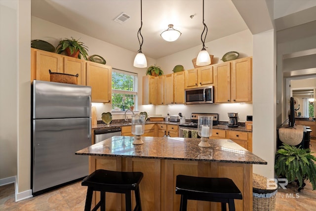 1430 Regency Rd Unit C103, Gulf Shores, AL 36542 - kitchen with appliances with stainless steel finishes, light brown cabinets, a breakfast bar area, dark stone countertops, and a kitchen island