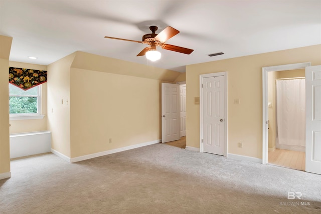 unfurnished bedroom featuring ceiling fan, light colored carpet, and ensuite bath