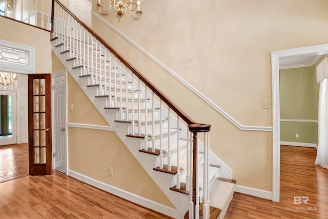 stairs with an inviting chandelier, crown molding, a high ceiling, and hardwood / wood-style flooring