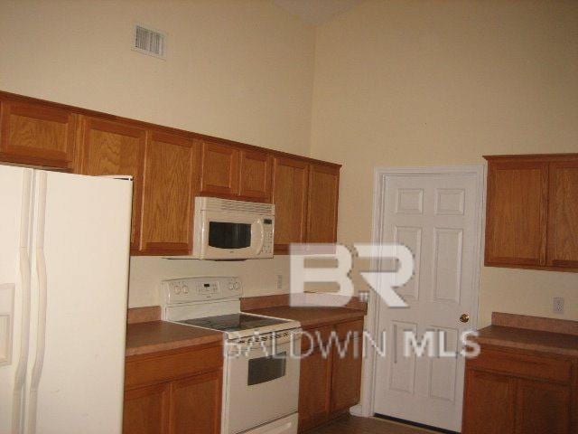 kitchen featuring visible vents, white appliances, a towering ceiling, and brown cabinetry