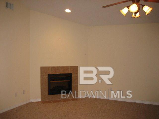 interior space featuring a tile fireplace, ceiling fan, and carpet flooring