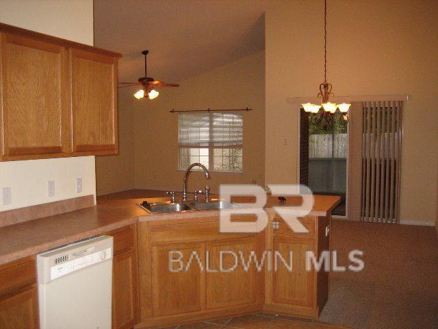 kitchen featuring brown cabinets, ceiling fan with notable chandelier, a sink, white dishwasher, and lofted ceiling