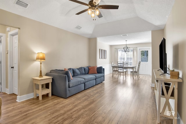 living area featuring a textured ceiling, light wood-style flooring, visible vents, a ceiling fan, and vaulted ceiling