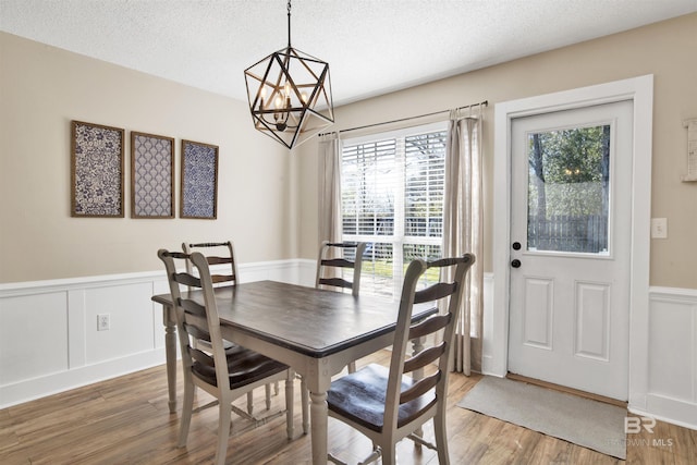 dining area with wainscoting, a notable chandelier, a textured ceiling, and light wood finished floors