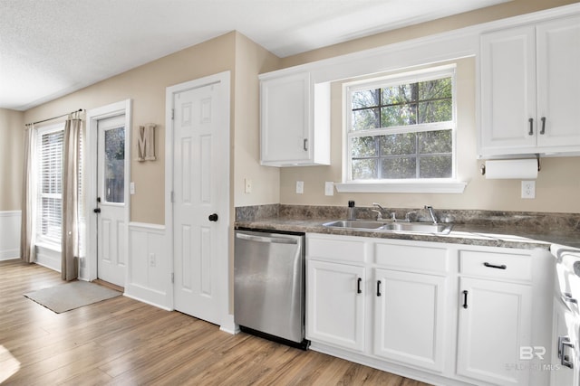 kitchen with a wainscoted wall, a sink, white cabinetry, stainless steel dishwasher, and light wood-type flooring