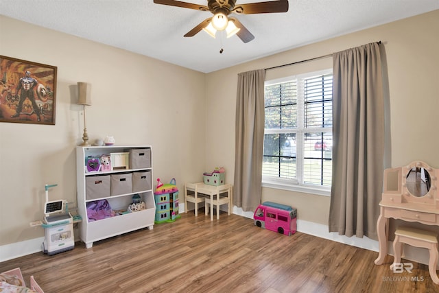 rec room featuring a ceiling fan, a textured ceiling, baseboards, and wood finished floors