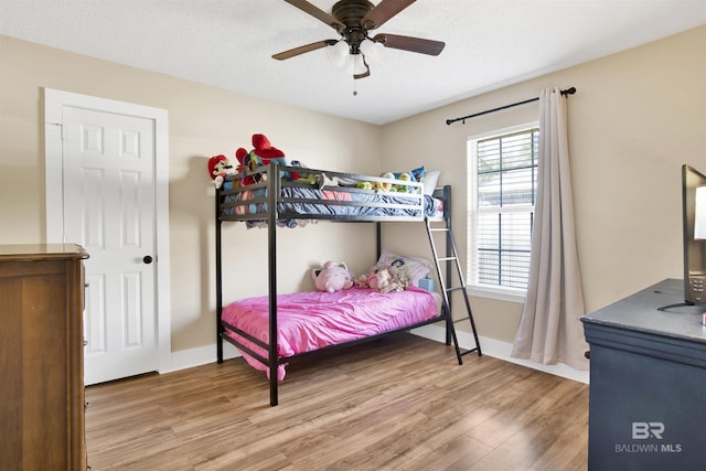 bedroom featuring a ceiling fan, a textured ceiling, baseboards, and wood finished floors