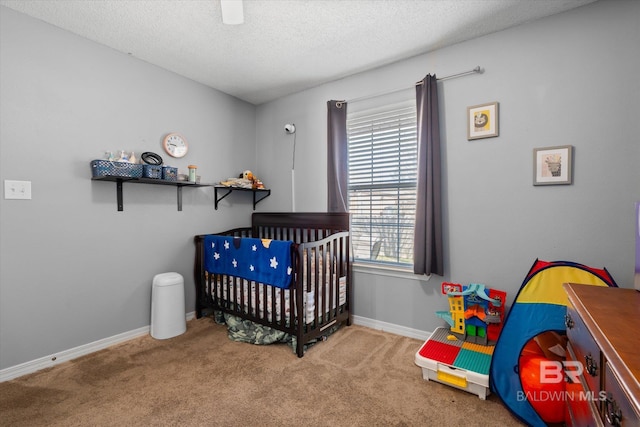 carpeted bedroom with a nursery area, a textured ceiling, baseboards, and a ceiling fan