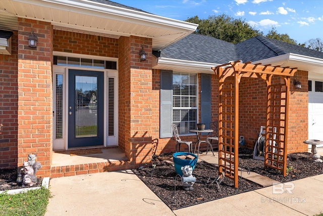 doorway to property featuring an attached garage, brick siding, and a shingled roof