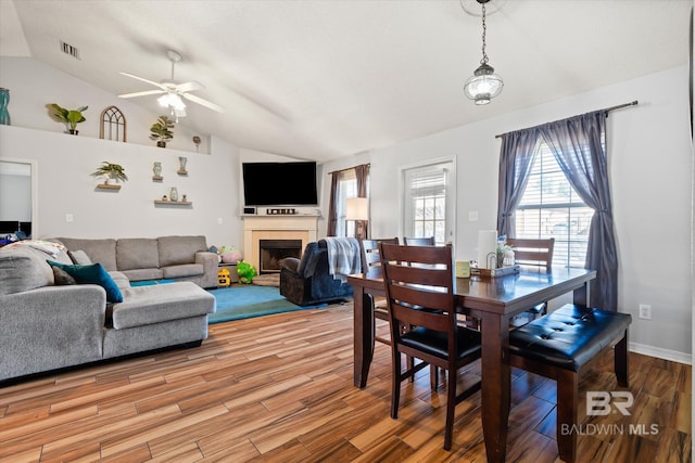 dining area featuring a ceiling fan, visible vents, lofted ceiling, a tiled fireplace, and light wood-type flooring