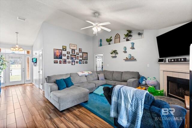 living area with visible vents, ceiling fan with notable chandelier, a tile fireplace, wood finished floors, and a textured ceiling