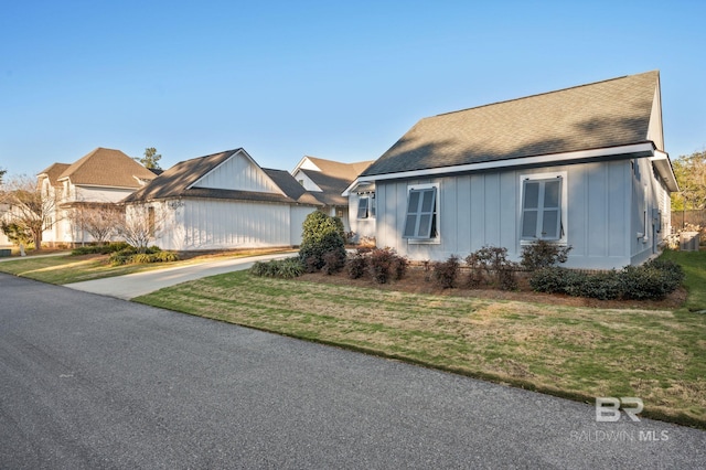 view of front of home with board and batten siding, a shingled roof, driveway, and a front lawn