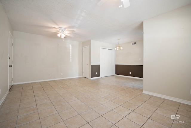 tiled spare room with a barn door, a textured ceiling, and ceiling fan with notable chandelier