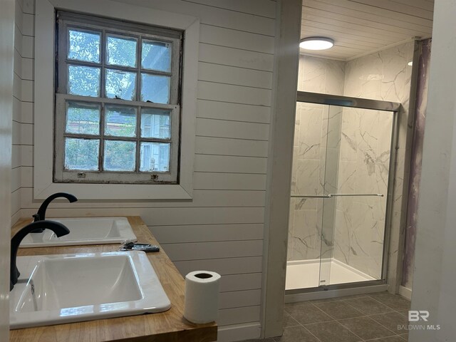 full bathroom featuring a marble finish shower, tile patterned flooring, a sink, and wooden walls