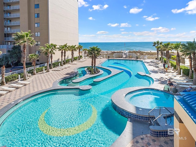 view of swimming pool with a water view, a patio area, a pool with connected hot tub, and fence