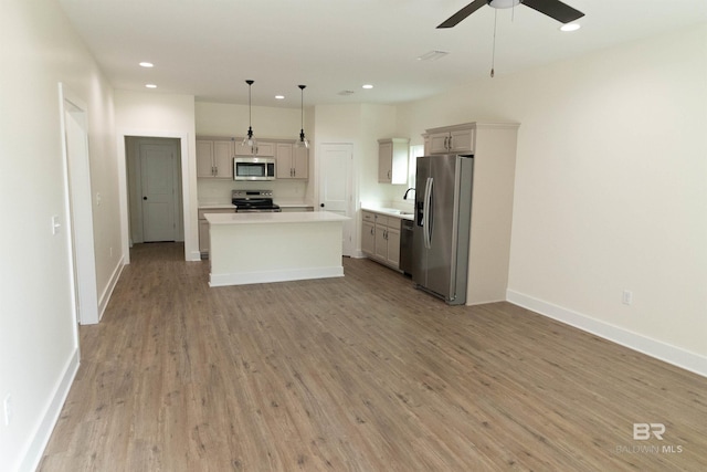 kitchen featuring ceiling fan, appliances with stainless steel finishes, decorative light fixtures, a kitchen island, and light wood-type flooring