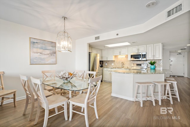 dining space with a chandelier, visible vents, light wood-style flooring, and baseboards