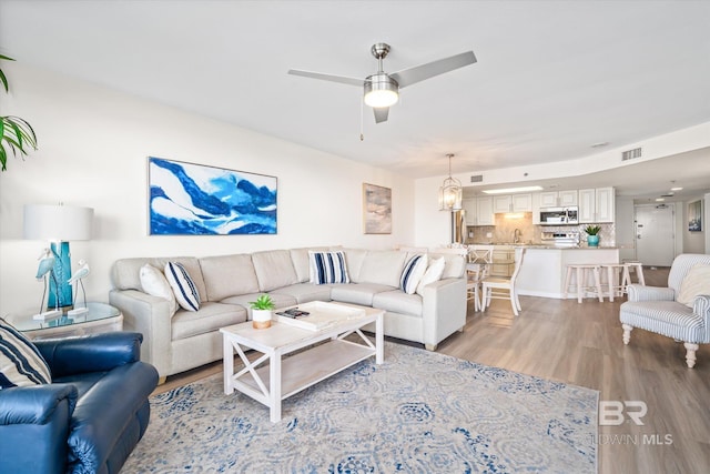 living room featuring visible vents, light wood-style flooring, and a ceiling fan