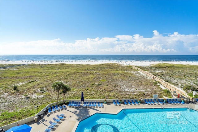 community pool with a water view, a patio, and a view of the beach