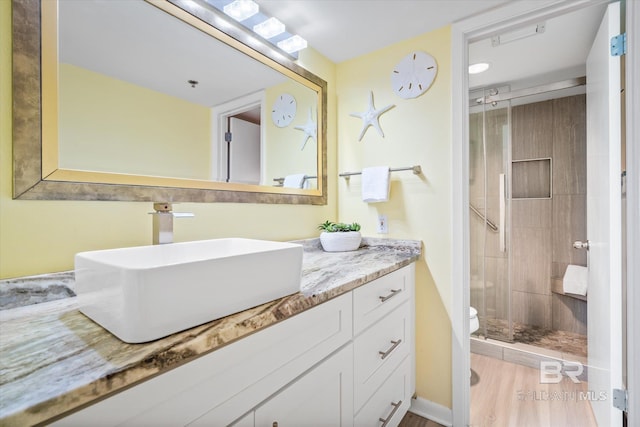 bathroom featuring vanity, toilet, wood finished floors, and a stall shower