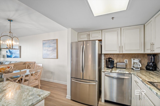 kitchen with light stone countertops, baseboards, light wood-style flooring, stainless steel appliances, and decorative backsplash