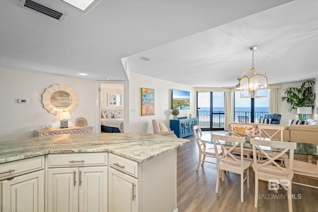 kitchen featuring light stone counters, visible vents, light wood-type flooring, decorative light fixtures, and open floor plan