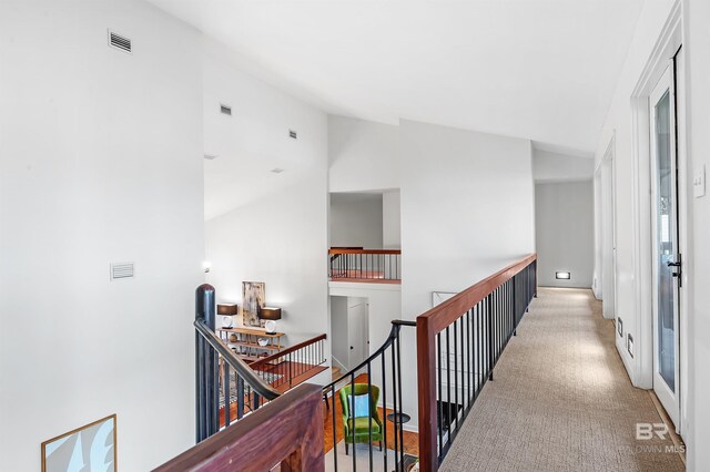 corridor with lofted ceiling, carpet floors, visible vents, and an upstairs landing