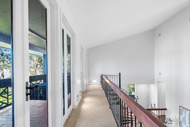 hallway featuring lofted ceiling, french doors, an upstairs landing, and light colored carpet