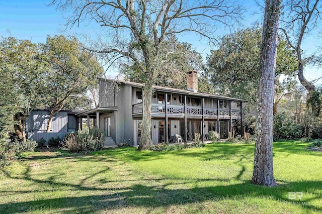 back of property featuring a balcony, a chimney, and a lawn