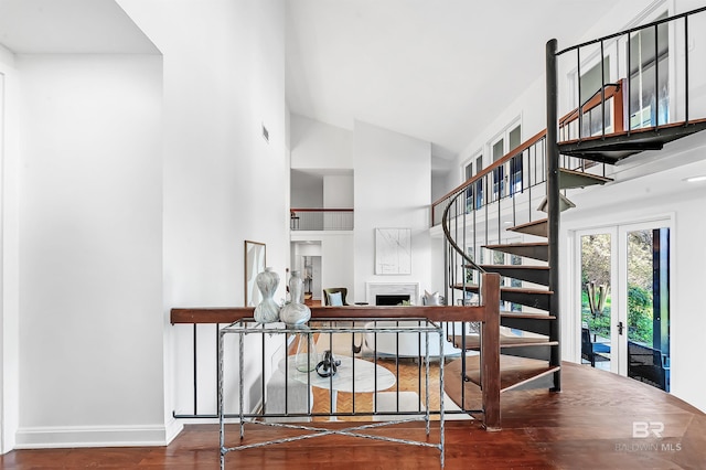 staircase with high vaulted ceiling, a fireplace, wood finished floors, visible vents, and baseboards