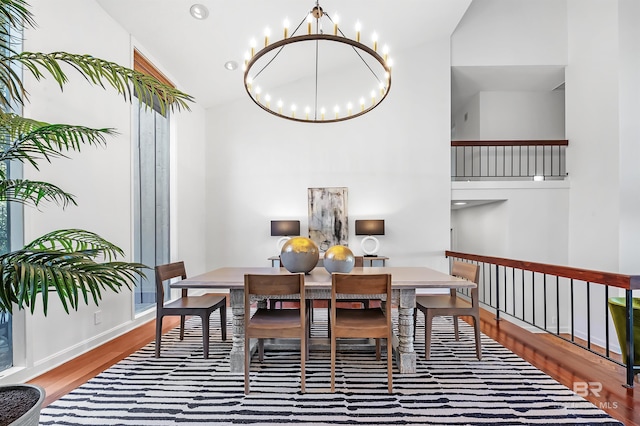 dining area with baseboards, high vaulted ceiling, wood finished floors, and a notable chandelier