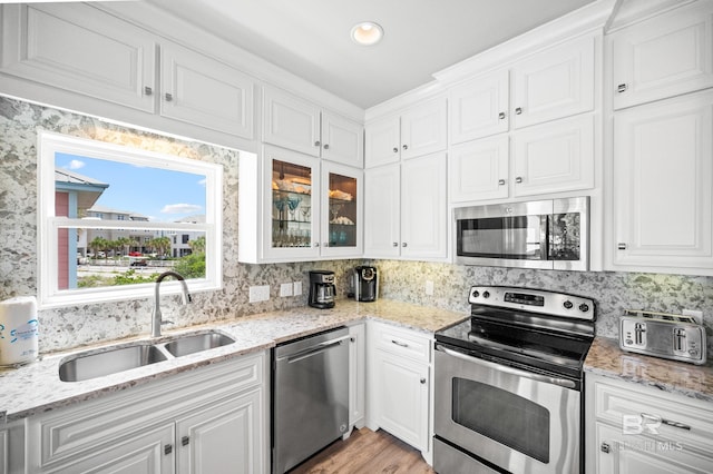 kitchen featuring a sink, stainless steel appliances, white cabinets, glass insert cabinets, and tasteful backsplash