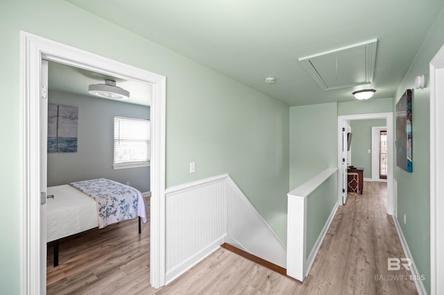 hallway featuring attic access, light wood-style flooring, an upstairs landing, and wainscoting