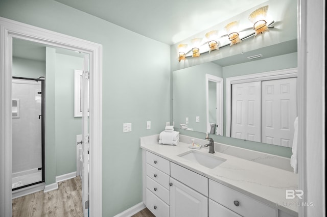 bathroom featuring visible vents, wood finished floors, a shower stall, baseboards, and vanity