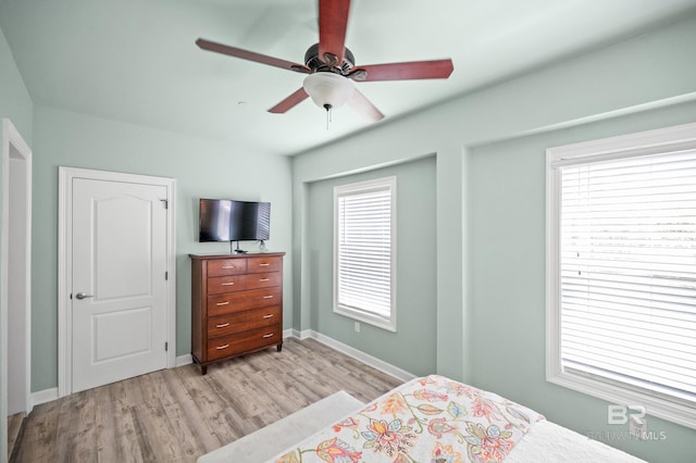 bedroom with light wood finished floors, multiple windows, baseboards, and ceiling fan