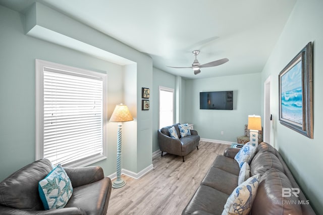 living room featuring a ceiling fan, baseboards, and light wood finished floors